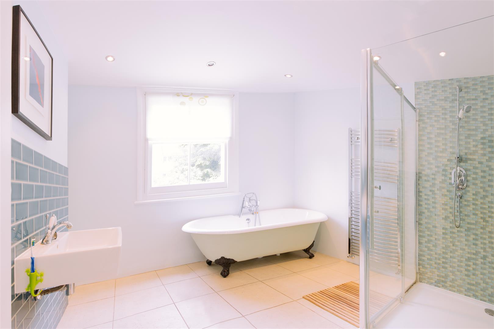 A picture of a large bright bathroom with a free standing bath, separate cubical shower and beautiful cream floor tiles. 